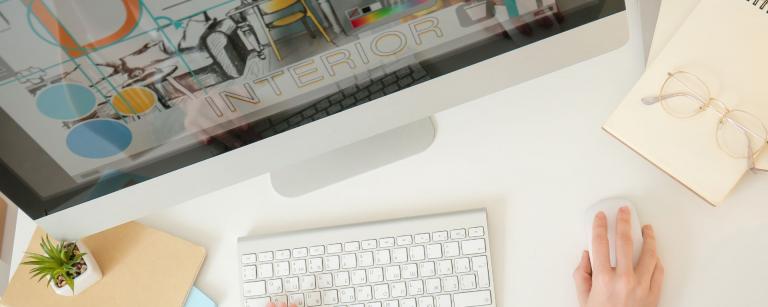 Imagen de computadora Mac con imagen de diseño sobre pantalla; escritorio blanco y mano sobre mousse